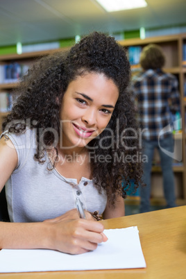 Student writing notes in notepad in the library