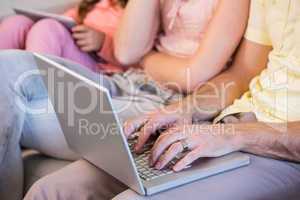 Family on couch using tablet pc and laptop