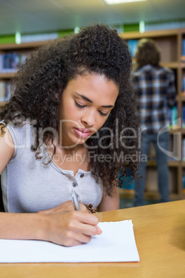 Student writing notes in notepad in the library