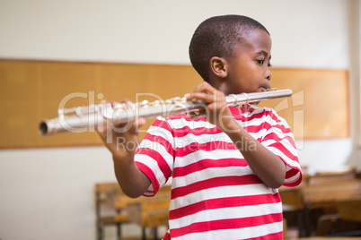 Cute pupil playing flute in classroom