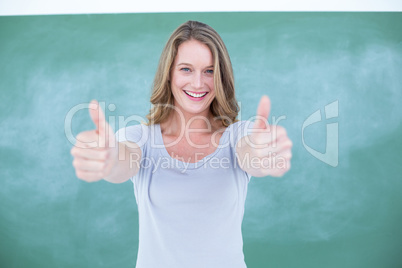 Smiling teacher standing thumbs up in front of blackboard