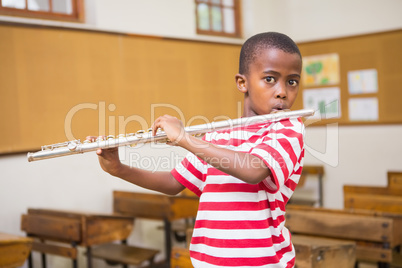 Cute pupil playing flute in classroom