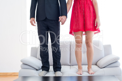 Geeky couple standing hand in hand on the couch