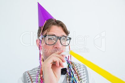 Geeky hipster wearing a party hat with blowing party horn