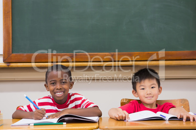 Cute pupils writing at desk in classroom