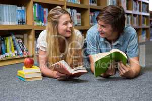 Students reading book lying on library floor