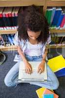 Student sitting on floor in library using laptop