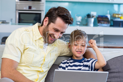 Father and son using laptop on the couch