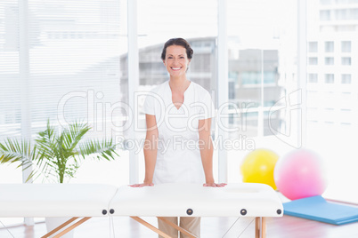 Smiling doctor looking at camera standing behind massage table