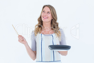 Smiling woman holding frying pan and wooden spoon