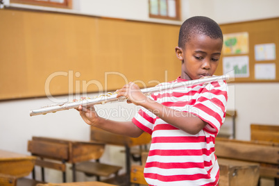 Cute pupil playing flute in classroom