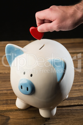 Hand putting heart in piggy bank