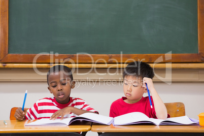 Cute pupils writing at desk in classroom