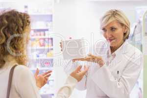 Pharmacist holding a bottle of drugs talking to customer