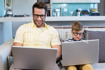 Father and son using laptops on the couch