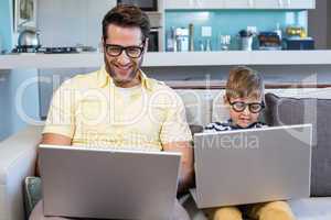 Father and son using laptops on the couch