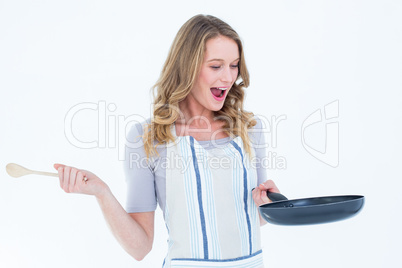 Smiling woman holding frying pan and wooden spoon