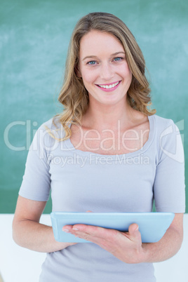 Smiling teacher holding tablet pc in front of blackboard