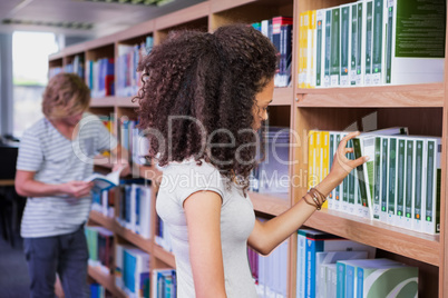 Student picking a book from shelf in library