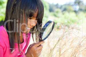 Cute little girl using magnifying glass in park