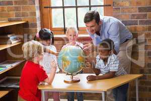 Cute pupils and teacher looking at globe in library