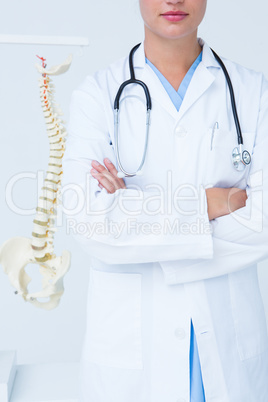 Doctor with arms crossed with anatomical spine behind