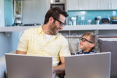 Father and son using laptops on the couch