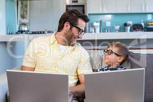 Father and son using laptops on the couch