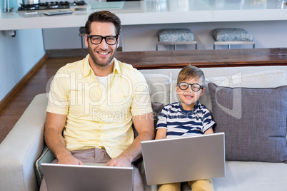 Father and son using laptops on the couch