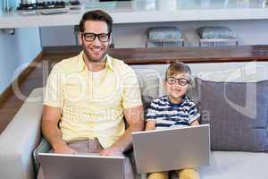 Father and son using laptops on the couch