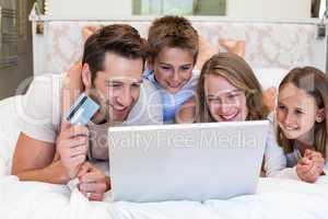 Happy family on the bed using laptop