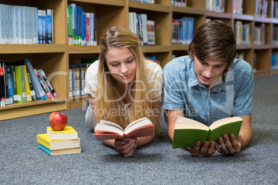 Students reading book lying on library floor