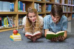 Students reading book lying on library floor