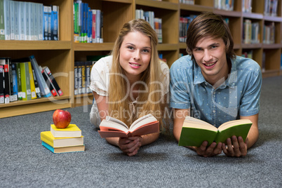 Students reading book lying on library floor