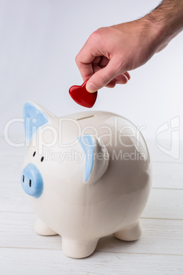 Hand putting heart in piggy bank