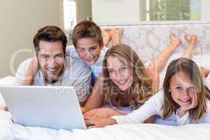 Happy family on the bed using laptop