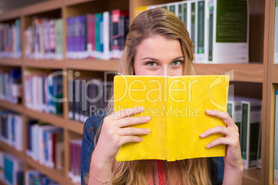 Student covering face with book in library