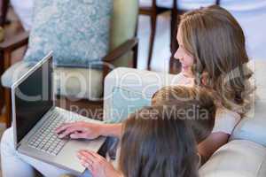 Mother and children using laptop on couch