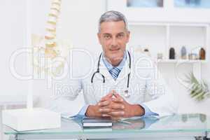 Doctor sitting at his desk smiling at camera