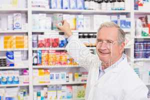Smiling pharmacist taking medicine from shelf