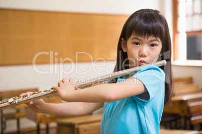 Cute pupil playing flute in classroom