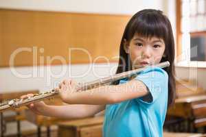 Cute pupil playing flute in classroom