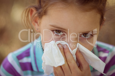 Cute little girl blowing her nose in park