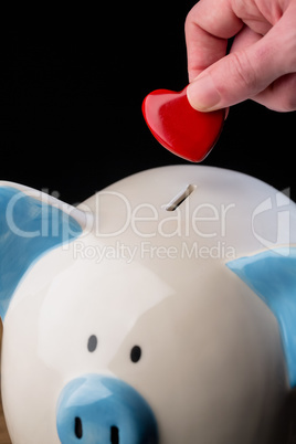 Hand putting heart in piggy bank