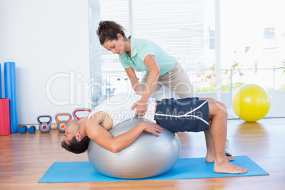 Trainer helping man with exercise ball