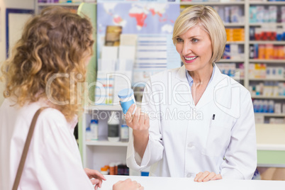Pharmacist showing medicine jar to costumer