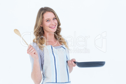 Smiling woman holding frying pan and wooden spoon