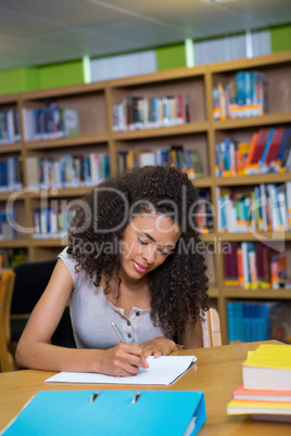 Student writing notes in notepad in the library