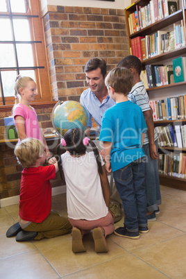 Cute pupils and teacher looking at globe in library