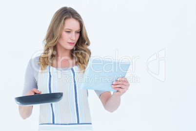 Concentrated woman holding frying pan and tablet pc